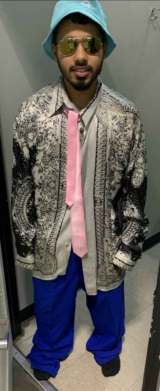 Zegoji in a bucket hat, gold aviators, patterned shirt, pink tie and blue pants